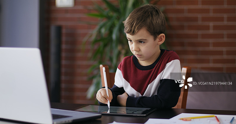 男孩在笔记本电脑上观看在线教程，并使用数位笔和数位板绘制数字图画。图片素材