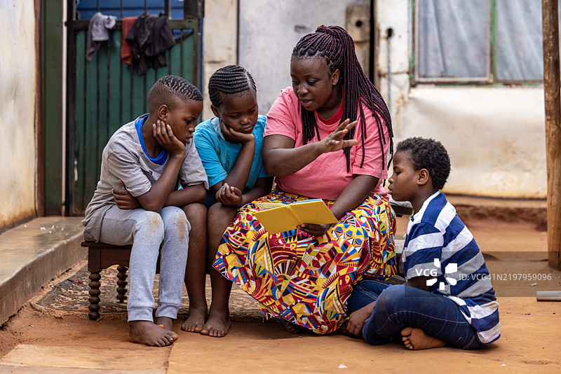贫困。不平等。一位黑人非洲女性在非洲的贫民区里给她的三个小孩读书。图片素材