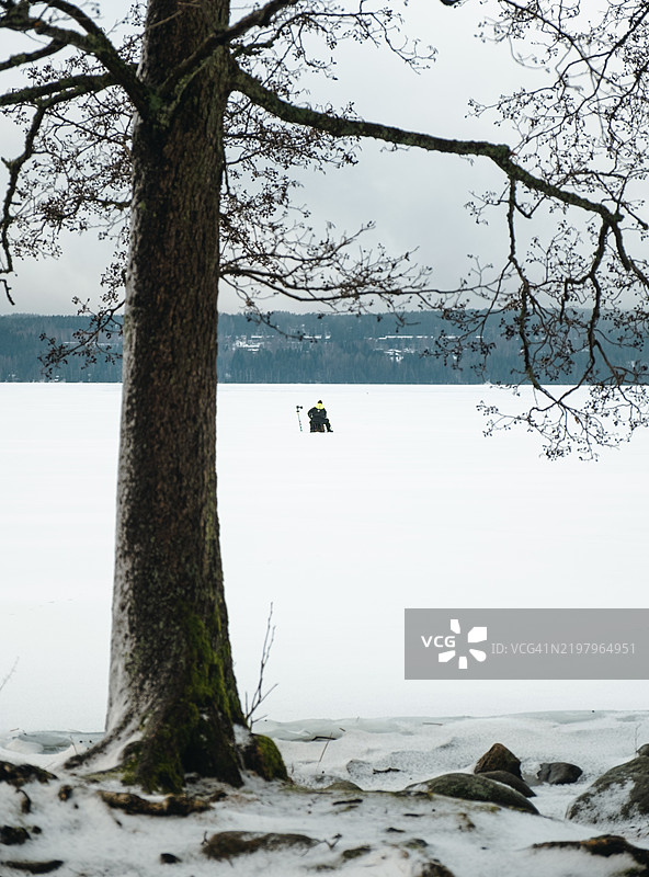冬季钓鱼。男人在冰冻湖面上钓鱼，冬季风景。湖岸线。图片素材