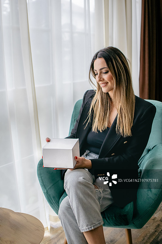 年轻的女博主坐在家中的办公室里，展示礼品盒，宣传产品，与摄像机对话，录制视频。图片素材