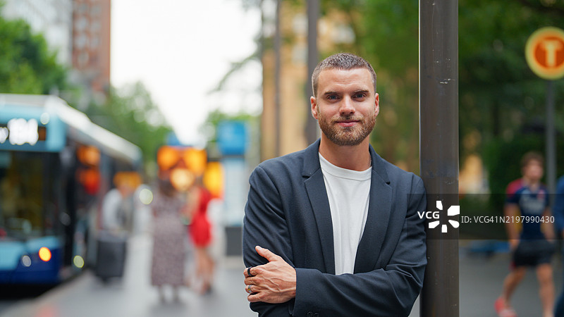 自信的年轻商人在繁忙的城市街道旁站立图片素材