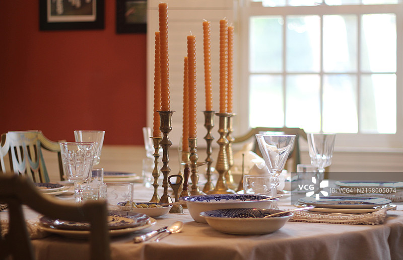 节日餐桌上摆放着收集的复古餐具、银器和烛台。古董蓝白瓷器搭配二手的纯银餐具。各种黄铜烛台装饰着餐桌。庆祝活动和节日餐宴。图片素材