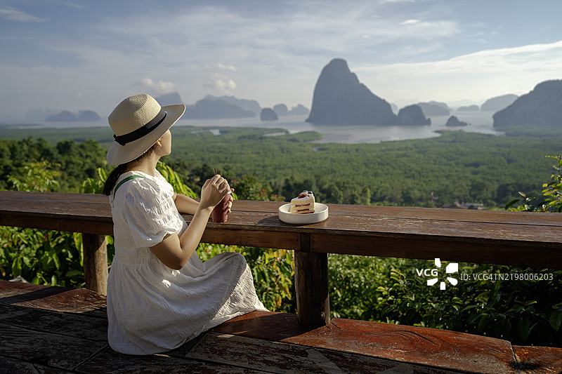 穿着裙子的女性坐着，欣赏泰国攀牙府萨美特南希岛观景点的阳光山景。图片素材