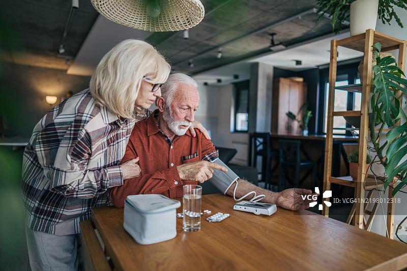 一位老年男性正在使用数字血压监测仪测量血压。图片素材