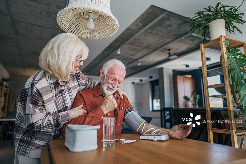 快乐的老年夫妇在家测量血压。图片素材