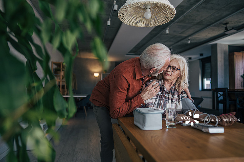 一位年长女性正在测量血压。她的丈夫在旁边紧张地注视着屏幕。她焦虑地看着读数，脸上露出不适的表情。图片素材