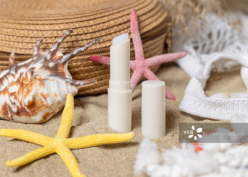 在沙滩上，阳光下的防晒唇膏棒与海星和贝壳相伴，化妆品展示图图片素材