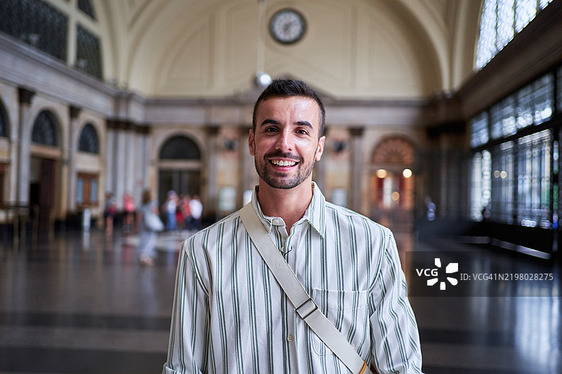 年轻男子在历史悠久的火车站建筑内部微笑。图片素材