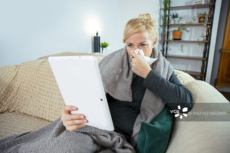 女人在客厅里擤鼻涕并使用平板电脑图片素材