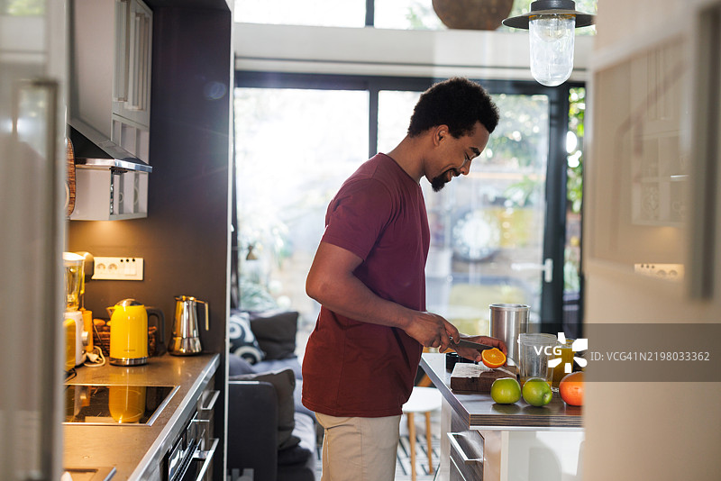 侧面视图的男子在现代明亮的厨房内准备新鲜水果图片素材