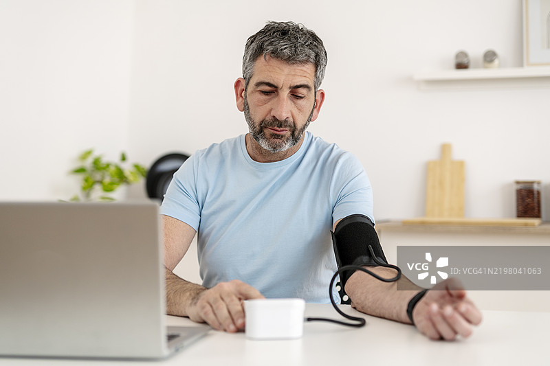 中年男子在虚拟医疗咨询中使用数字血压监测仪测量血压，代表远程医疗健康监测。图片素材