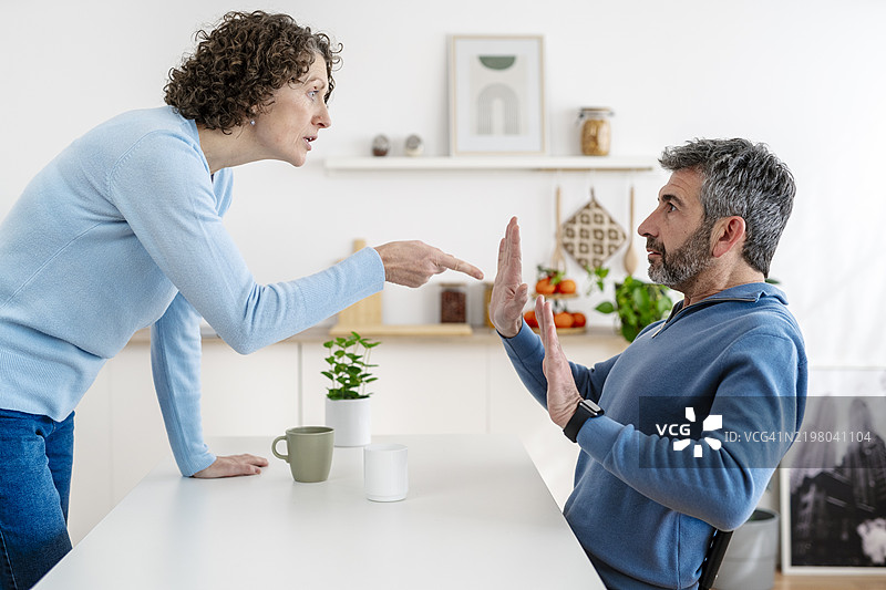 成熟夫妇在厨房争吵，女人用手指指着抬起双手的男人图片素材