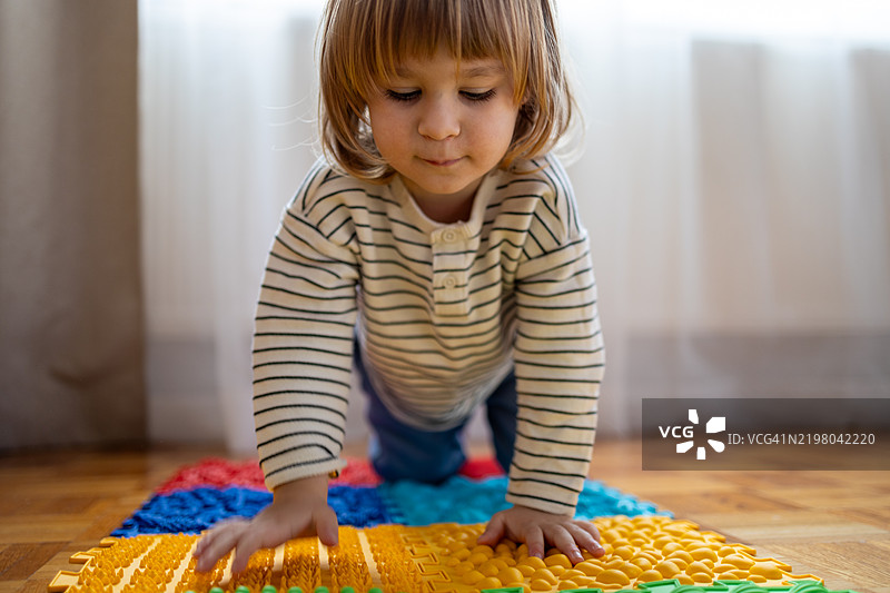好奇的小男孩坐在木地板上的按摩垫上图片素材