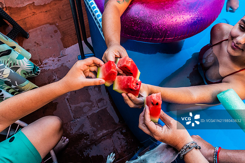 一家人在家里的泳池中开心地举着西瓜干杯的特写镜头图片素材