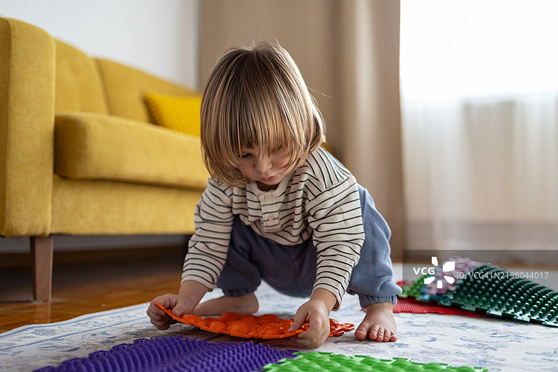 小男孩在木地板上搭建按摩垫。预防扁平足在家中进行。图片素材