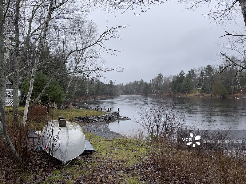 在雨天的宁静河边，前景中有一只小艇。图片素材