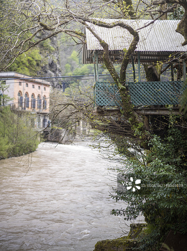 俯瞰河流的木制树屋，四周环绕着郁郁葱葱的绿树和乡村风格的建筑图片素材
