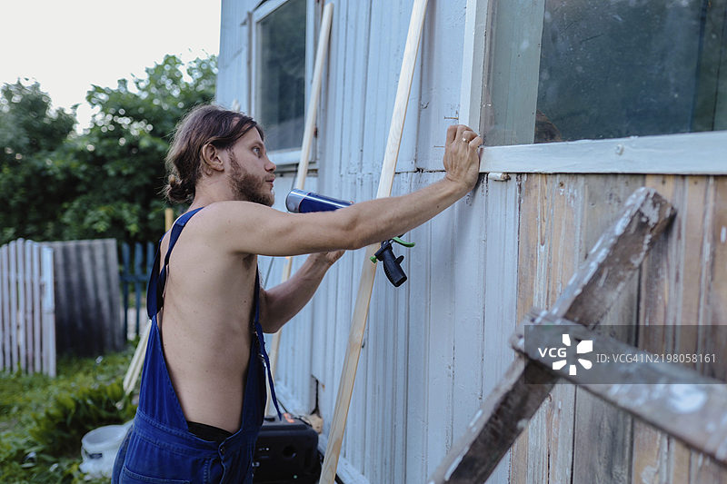 一名男子在房屋翻新时密封窗框，手持填缝枪图片素材