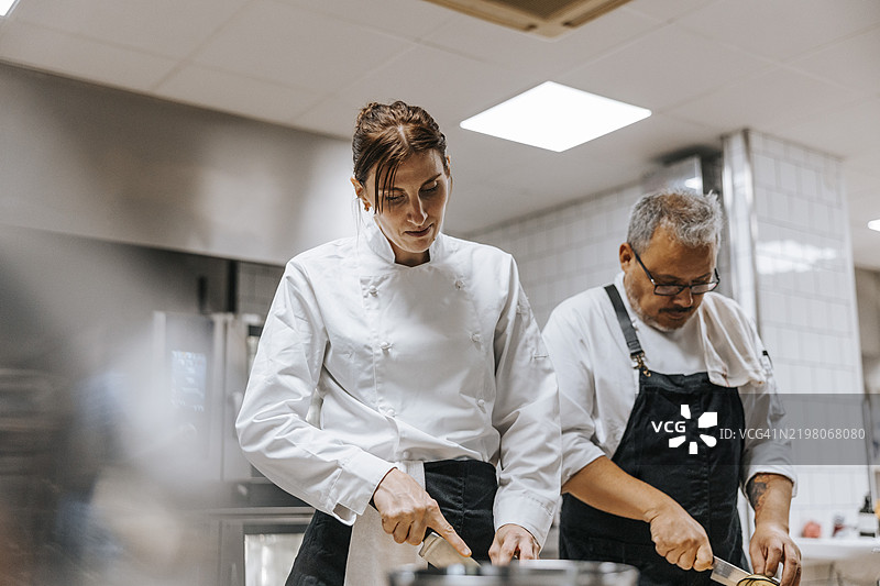 低角度视图的女厨师和男厨师在餐厅厨房工作时切菜图片素材