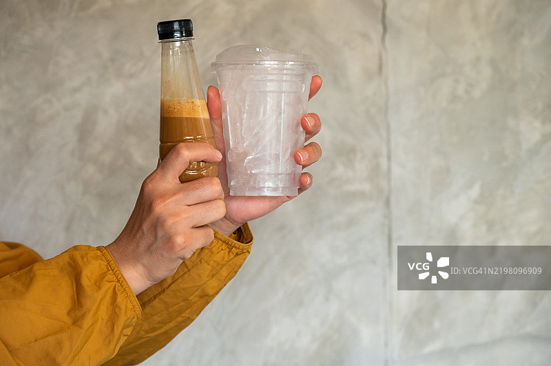 女人手中拿着装有冰块的塑料杯和塑料瓶的奶咖啡，画面为裁剪视角。图片素材