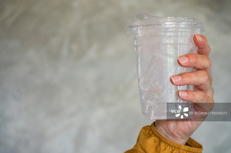 一个人手里拿着装满冰块的塑料杯，放在桌子上。图片素材