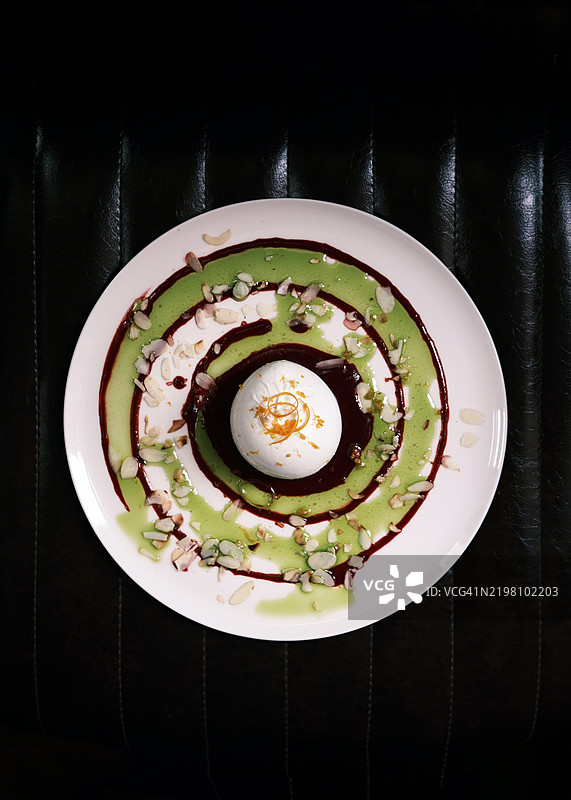 从上方俯视装盘的布拉塔奶酪，配有罗勒香蒜酱、香醋减汁和碎坚果，白色盘子，优雅的意大利餐厅环境，背景昏暗。图片素材