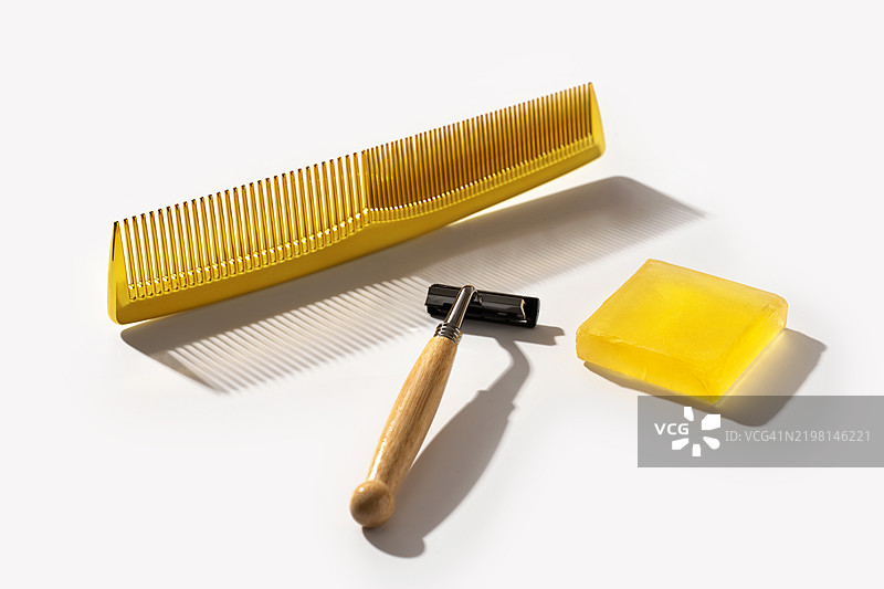 男性日常美容护肤概念，包含白色桌面上的美容产品，剃须刀、金棕色梳子和一块香皂。图片素材