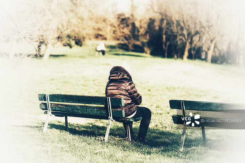 穿着夹克的人坐在公园的公共长椅上休息图片素材