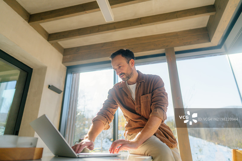 在小木屋里使用笔记本电脑的男人图片素材