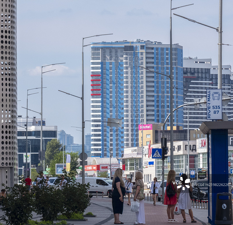 繁忙的城市街道上，行人们在阳光明媚的日子里享受着现代建筑的生机勃勃的城市风景。图片素材