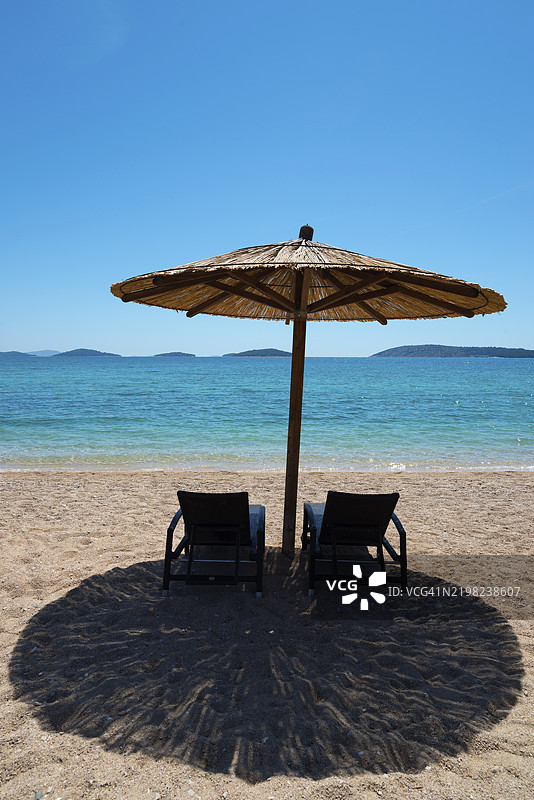一个安静的海滩场景，两个躺椅在海边的遮阳伞下，阿马德里亚公园，白沙滩，希贝尼克，希贝尼克-克宁，达尔马提亚，克罗地亚，欧洲图片素材