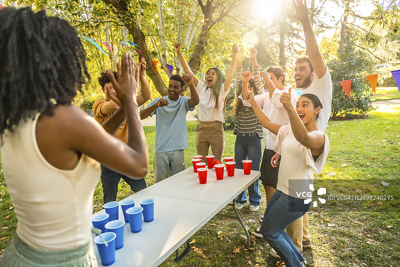 多种族的年轻朋友们祝贺一位赢得啤酒乒乓球比赛的非洲女性图片素材