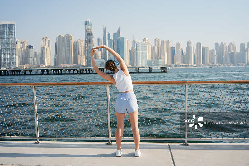 年轻女性在迪拜海滨天际线旁拉伸图片素材