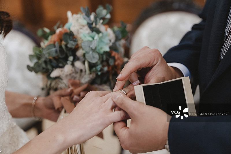 一对情侣在婚礼仪式上互换戒指的特写，背景中有美丽的花束，象征着爱与承诺。图片素材