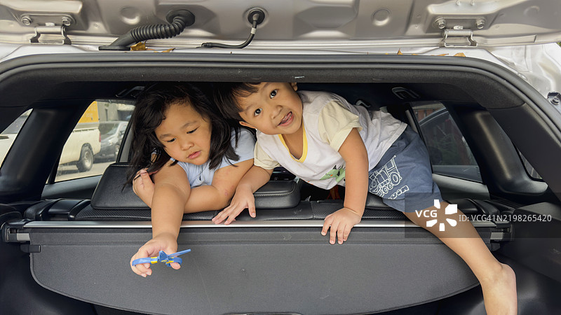 孩子们在汽车后备厢里快乐地玩耍，探索新的冒险。完美的家庭公路旅行时刻生动地被捕捉。适合儿童的旅行创意。图片素材