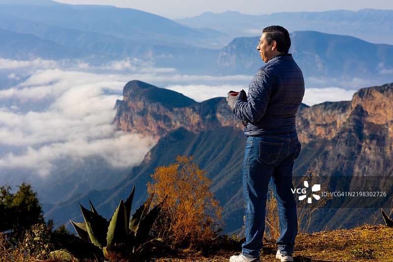 男人在山顶享受美景，手里拿着咖啡杯图片素材