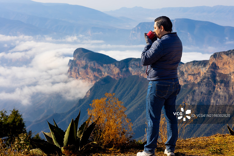 男人在山顶享受美景，手里拿着咖啡杯图片素材