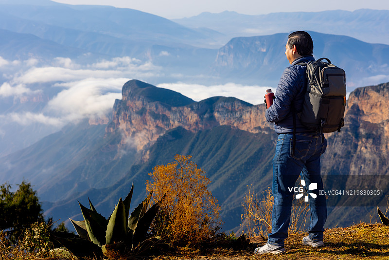 男人在山顶享受美景，手里拿着一瓶水图片素材