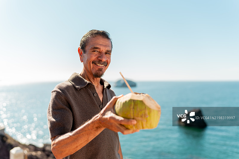 海岸线上喝椰子水的老年男性肖像图片素材