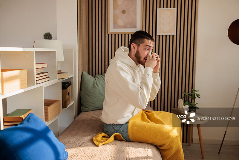 年轻男子在家中打电话，正在从感冒中恢复图片素材