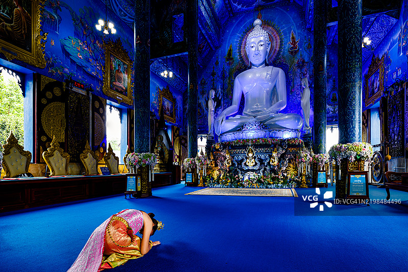 在泰国北部蓝庙前跪拜的女性。图片素材