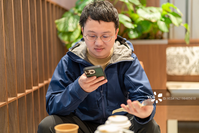 一位亚洲男子在咖啡店用手机付款，手中拿着账单。图片素材