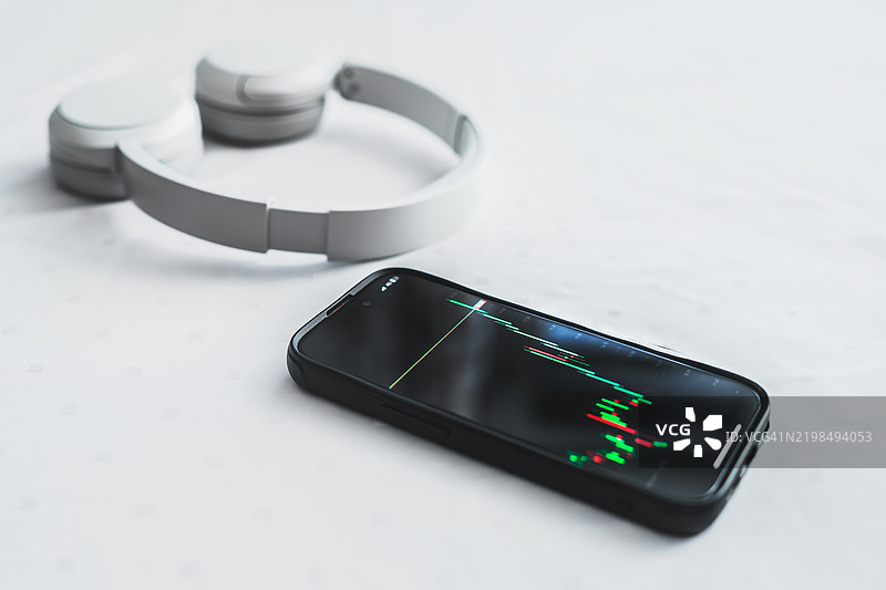 白色桌子上放着显示股票市场图表的智能手机和无线耳机图片素材