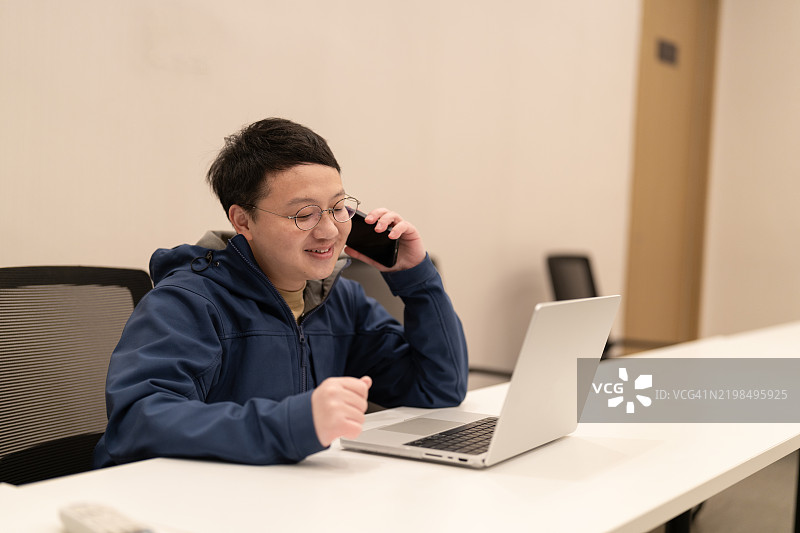 一位亚洲男子在会议室接电话，正看着电脑屏幕。图片素材