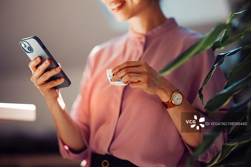 女性在轻松的环境中手持手机和咖啡杯图片素材