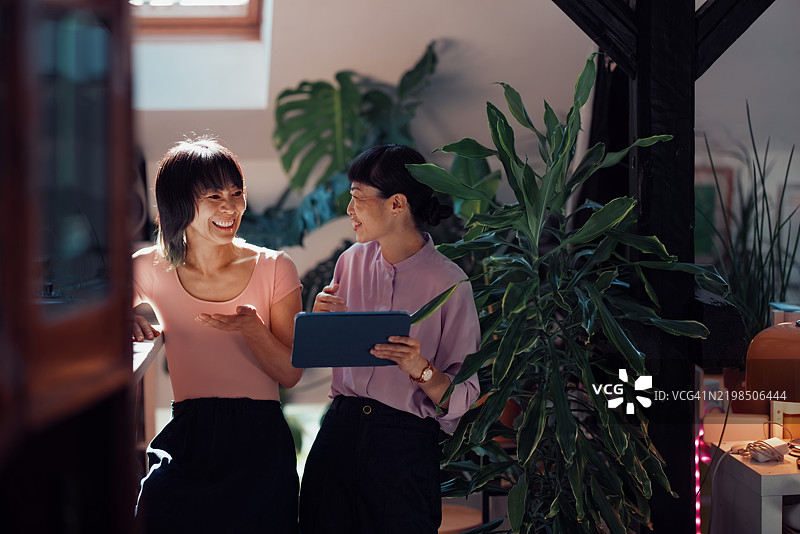 两位女性在明亮的绿色办公室环境中交谈图片素材