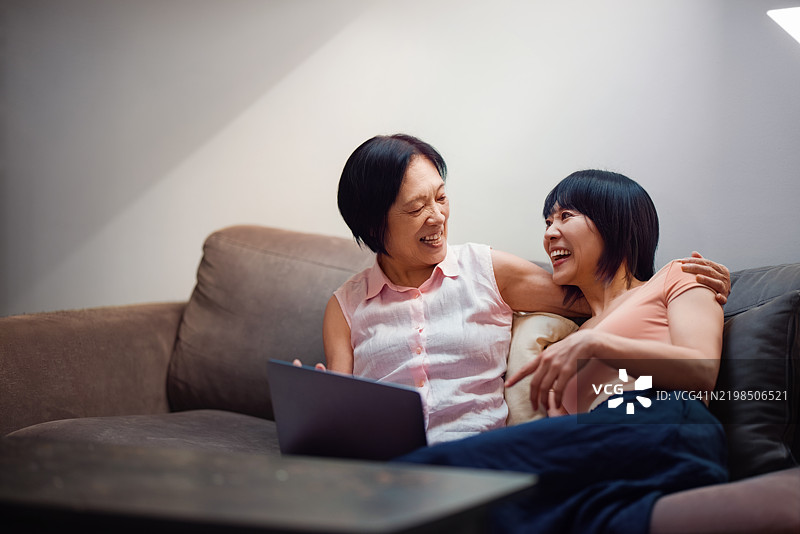 微笑的家庭在沙发上共享笑声，使用同一台笔记本电脑图片素材