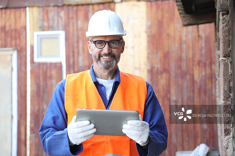 一位年长的男性白人建筑师、建筑承包商或工程师，在建筑工地上使用数字平板电脑的肖像图片素材