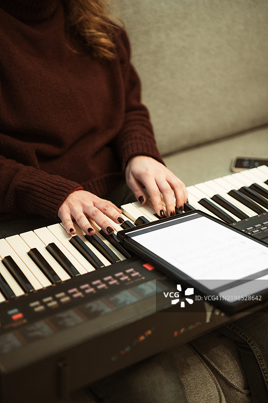 女性在合成器上创作音乐，同时在平板电脑上阅读乐谱图片素材