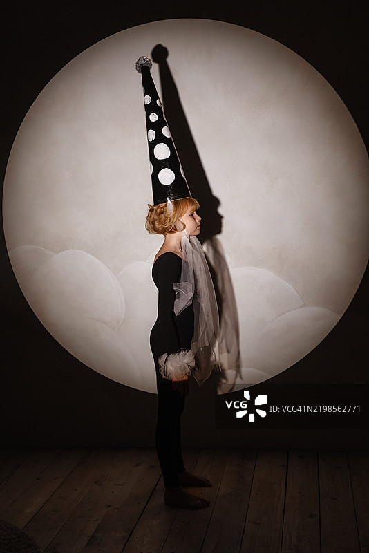 小女孩穿着皮埃罗服装在聚光灯下摆姿势。图片素材